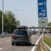 Auto met dakkoffer rijdt op een Europese snelweg langs borden voor tolwegen en milieuzones tijdens de zomervakantie